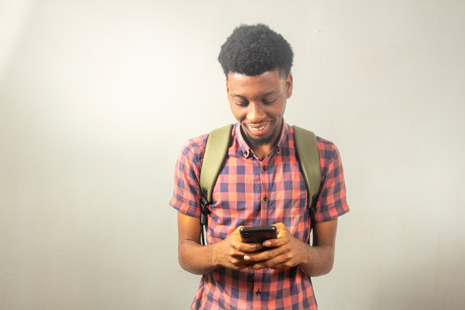 Teenage boy smiling while using a smartphone and carrying a backpack